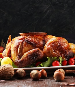 a table set for christmas dinner with a hot roasted turkey in the centre of a long wooden table  with pine cone decorations 