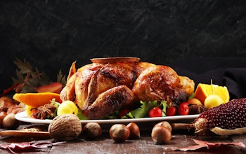 a table set for christmas dinner with a hot roasted turkey in the centre of a long wooden table  with pine cone decorations 