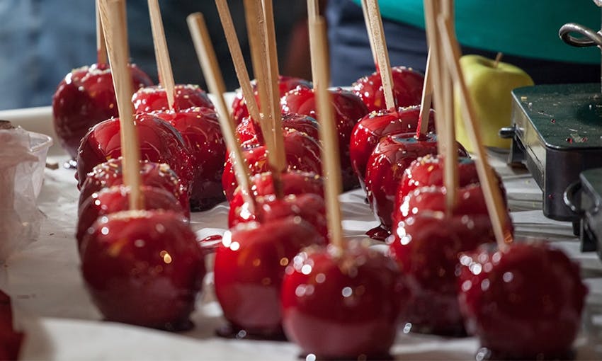 Dozens of Red Sticky toffee apples lined up on baking paper with sticks poked in middle 