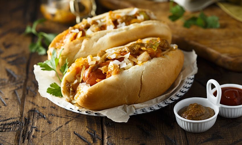 Hot dogs in crusty bread roll topped with a range of onions served with fresh herbs and dipping sauce 