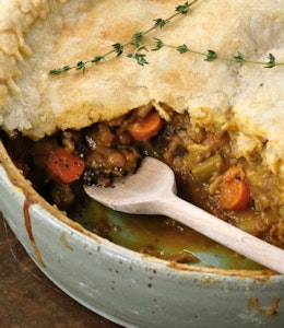 half open pie with hearty warming meat filling in a ramekin topped with a sprig of herbs