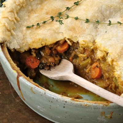 half open pie with hearty warming meat filling in a ramekin topped with a sprig of herbs