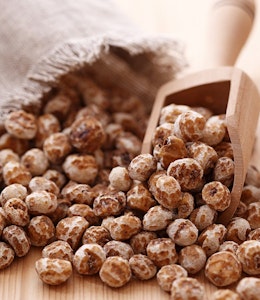 a bag of tiger nuts spilled out onto table with a small wooden rectangular scooper 