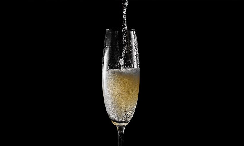 Prosecco glass in the centre of a black background with wine being poured from above 