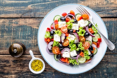 tasty greek salad of feta lettuce tomatoes red onion tomato cucumber and olives with a dressing and pepper grinder 