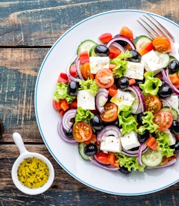 tasty greek salad of feta lettuce tomatoes red onion tomato cucumber and olives with a dressing and pepper grinder 