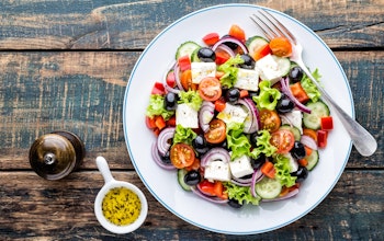 tasty greek salad of feta lettuce tomatoes red onion tomato cucumber and olives with a dressing and pepper grinder 