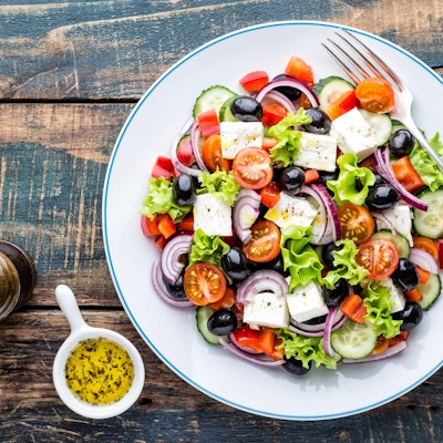 tasty greek salad of feta lettuce tomatoes red onion tomato cucumber and olives with a dressing and pepper grinder 