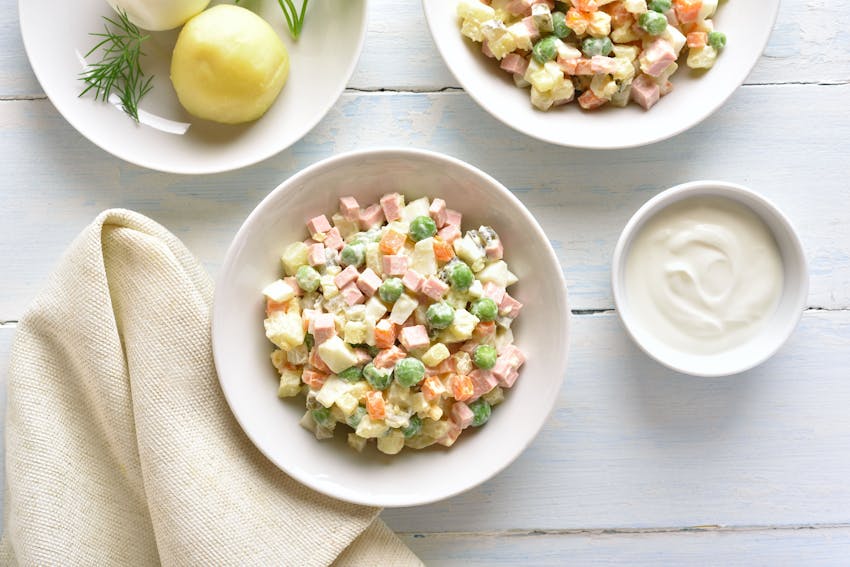 a bowl of diced boiled potatoes, carrots, dill pickles, eggs, peas, celeriac, onions, diced boiled chicken, tart apples, salt, pepper, mustard and mayonnaise