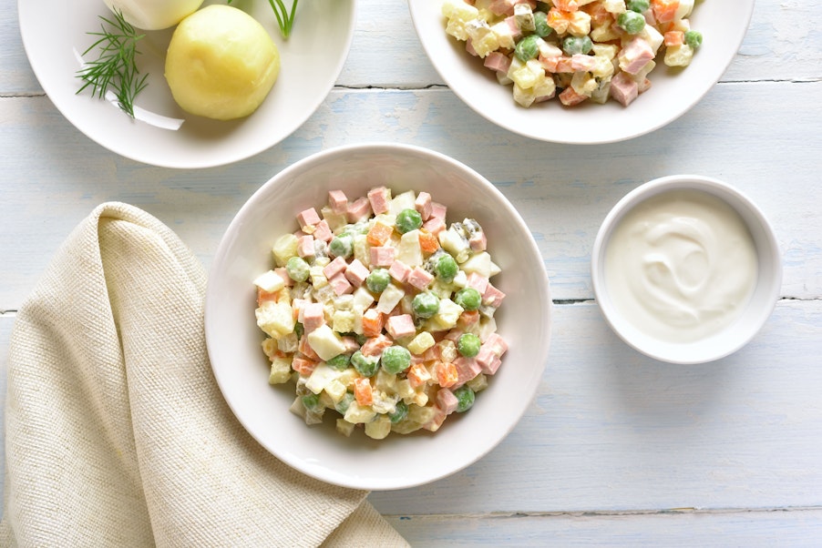 a bowl of diced boiled potatoes, carrots, dill pickles, eggs, peas, celeriac, onions, diced boiled chicken, tart apples, salt, pepper, mustard and mayonnaise
