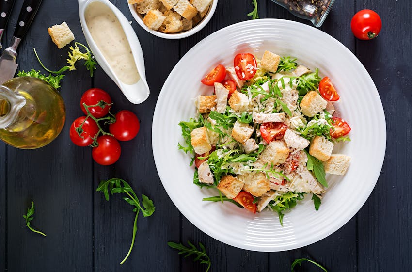 romaine lettuce croutons lemon juice olive eggs worcestershire sauce anchovies garlic dijon mustard parmesan cheese black pepper and chicken served on a white dish 