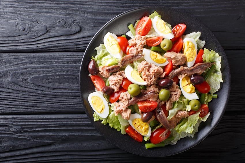 a plate of tomatoes hard boiled eggs nicoise olives anchovies cucumbers olive oil and tuna 