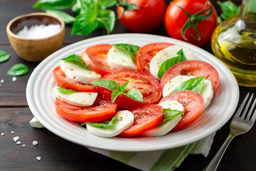 a plate of layered sliced mozerella and sliced tomatoes sweet basil olive oil and salt 