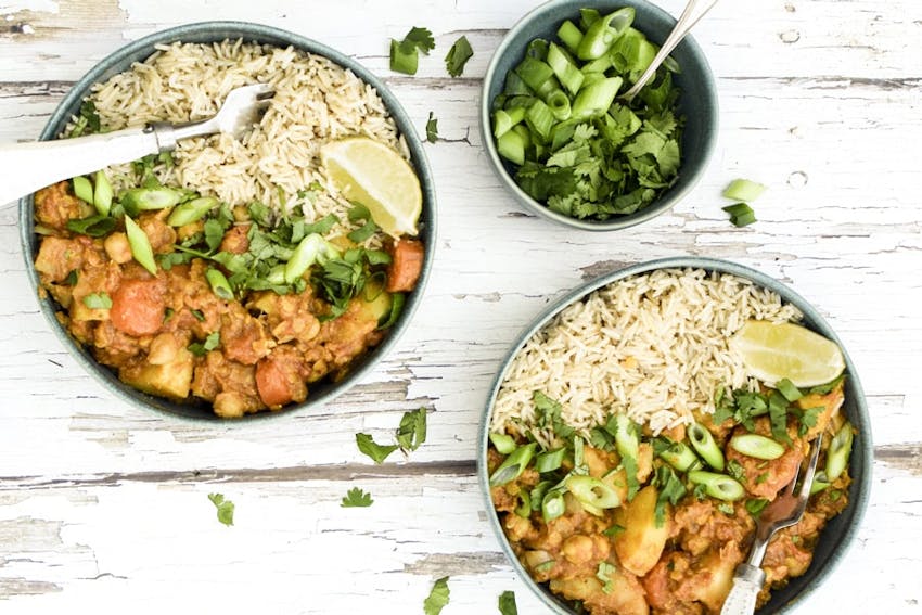 Two bowls of curried vegetable root casserole next to a small bowl of green onions on a wooden table 