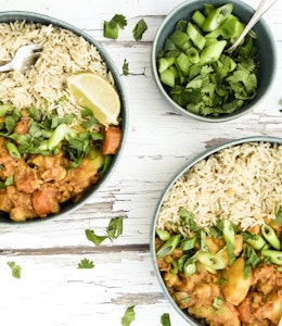 Curried Root Vegetable Casserole Two bowls of curried vegetable root casserole next to a small bowl of green onions on a wooden table