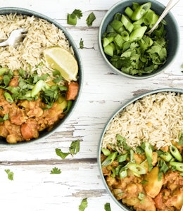 Two bowls of curried vegetable root casserole next to a small bowl of green onions on a wooden table 