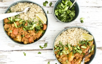 Two bowls of curried vegetable root casserole next to a small bowl of green onions on a wooden table 