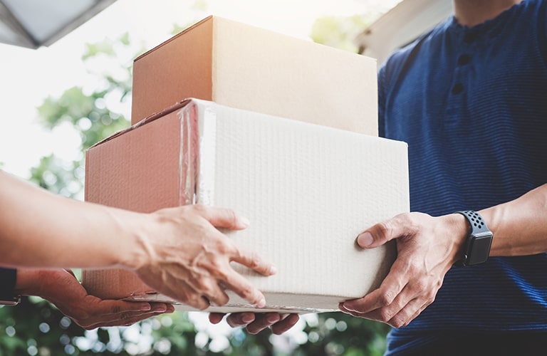 Man handing stacked cardboard boxes to another man who is wearing a blue tshirt and a watch 