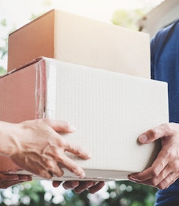 Man handing stacked cardboard boxes to another man who is wearing a blue tshirt and a watch 