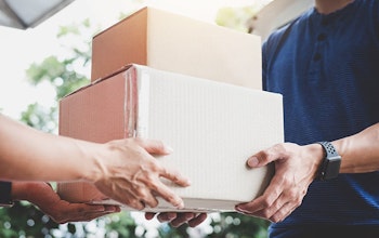 Man handing stacked cardboard boxes to another man who is wearing a blue tshirt and a watch 