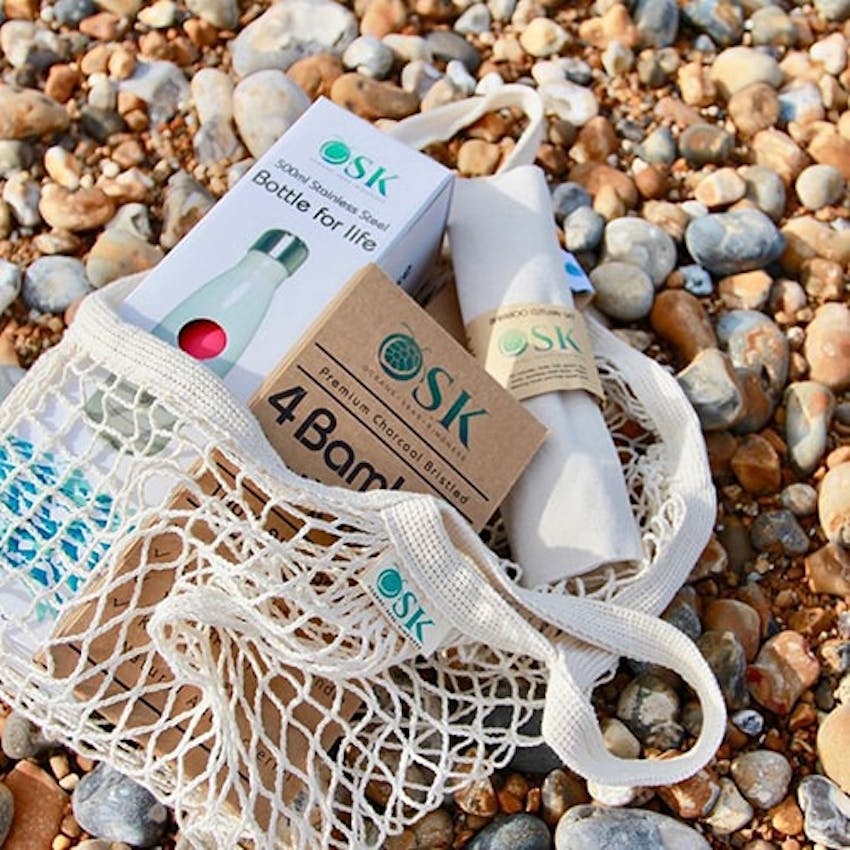 OSK Eco sustainable net bag with other eco friendly OSK products layed across a stony shingle on the beach 