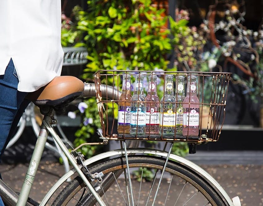 Man riding vintage bicycle outdoors with a range of buzbees tonics in the basket 