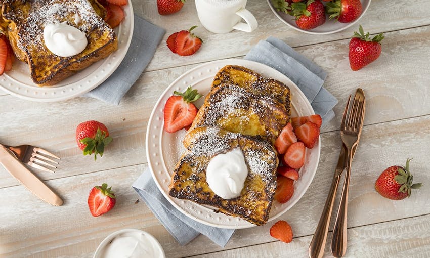 a breakfast spread of french brioche toast topped with icing sugar, cream and fresh strawberries 