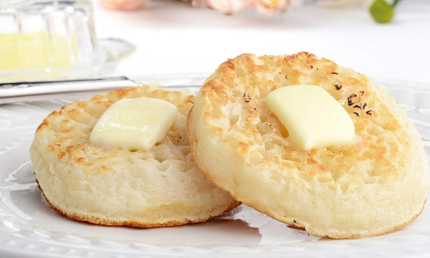 two crumpets with a knob of butter melting in the middle served on a white plate 