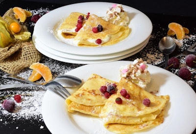 two plates of sweet crepes on a decorated table dusted with icing sugar and topped with berries 
