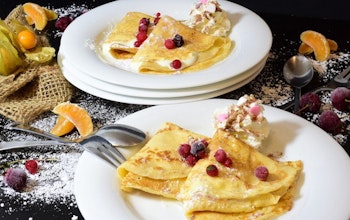 two plates of sweet crepes on a decorated table dusted with icing sugar and topped with berries 
