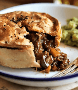 a crusty pie with a vegan mushroom tomato and red wine onion and thyme filling served with mushy peas 