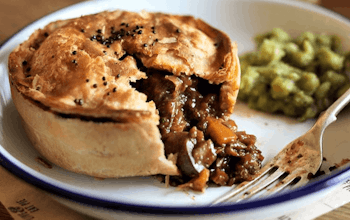 a crusty pie with a vegan mushroom tomato and red wine onion and thyme filling served with mushy peas 