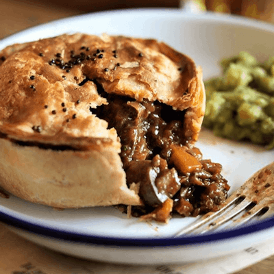 a crusty pie with a vegan mushroom tomato and red wine onion and thyme filling served with mushy peas 