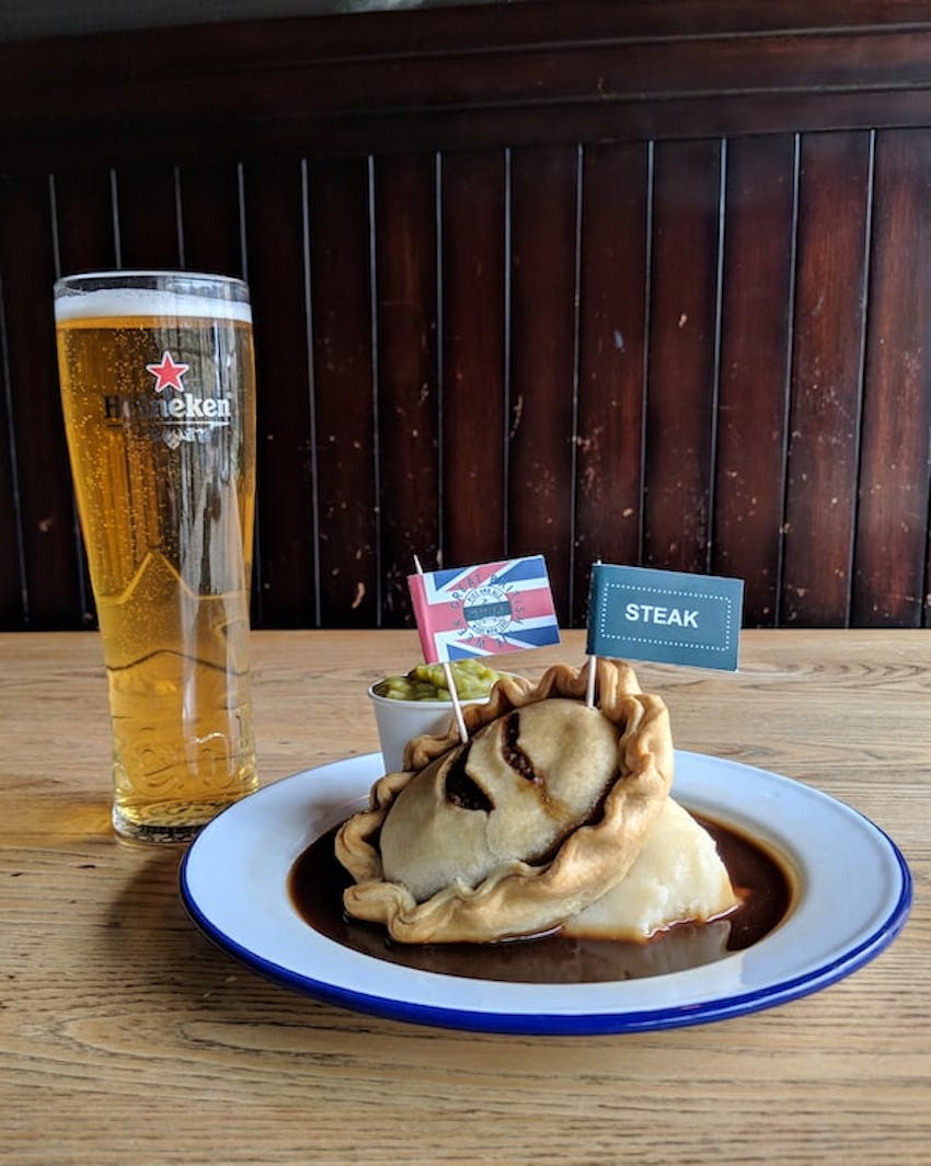 redhouse steak pie swimming in gravy with a side of peas and a heineken beer