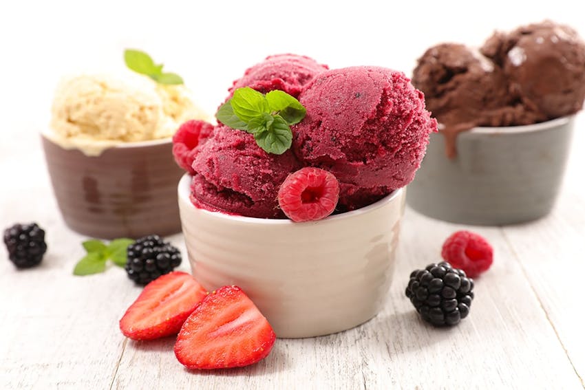 Vanilla, Raspberry and Chocolate ice cream pots with mint and fruit scattered around wooden table 