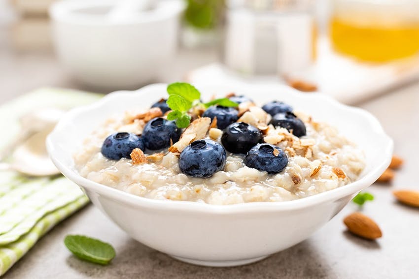 a bowl of creamy porridge topped with fresh blueberries almonds and sprigs of mint 