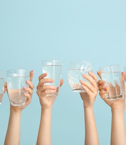 six hands holding up clear glasses of water 