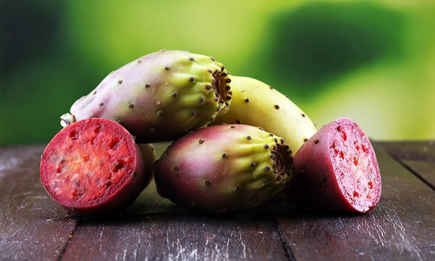 a pile of prickly pear cactus with two chopped in half to reveal pink and seeded inside 