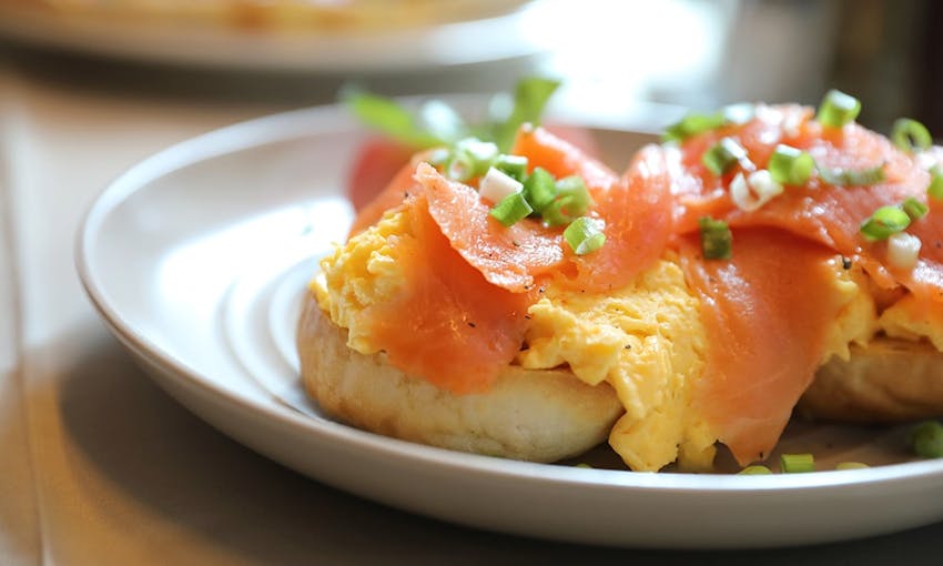 egg salmon and avocado bagel served on a white dish topped with diced spring onion 