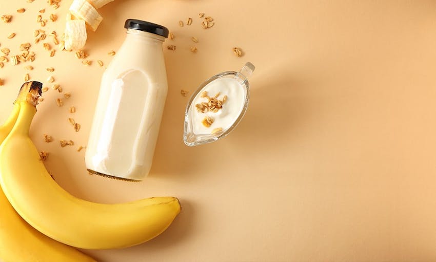 a bunch of bananas some sprinkled oats and a glass bottle of milk with a yellow background