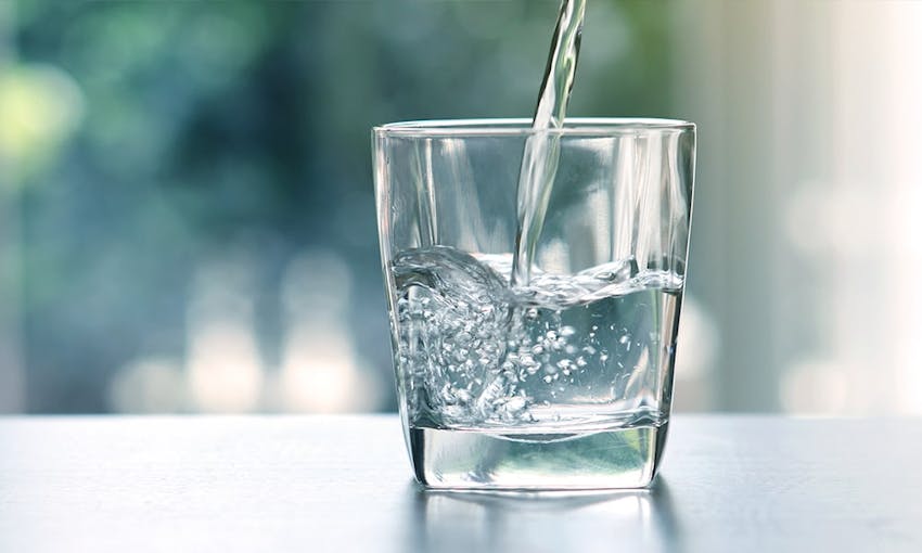 a glass of water on a tabletop with water being poured into it 