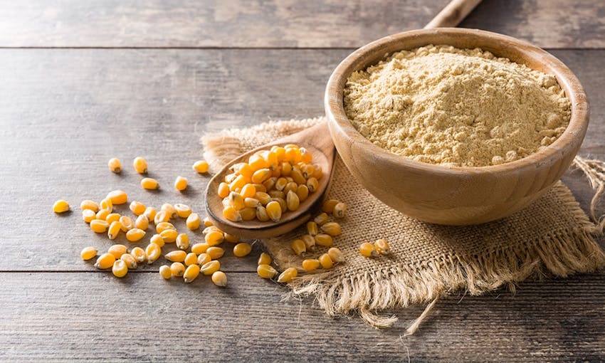 a small wooden bowl of grinded pea protein next to a wooden spoon with whole seeds of pea protein 