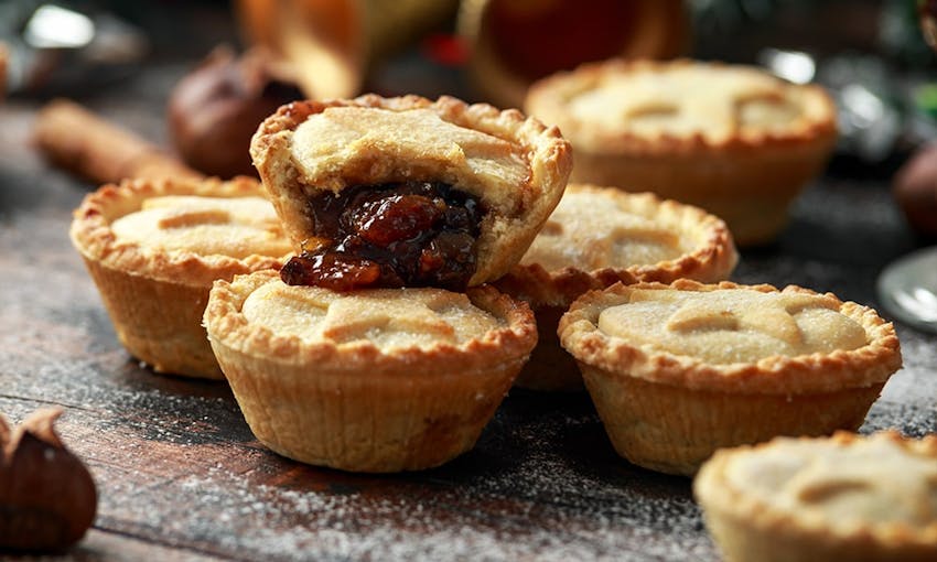 a stack of mince pies  on a dark wooden table with a dusting of icing sugar 