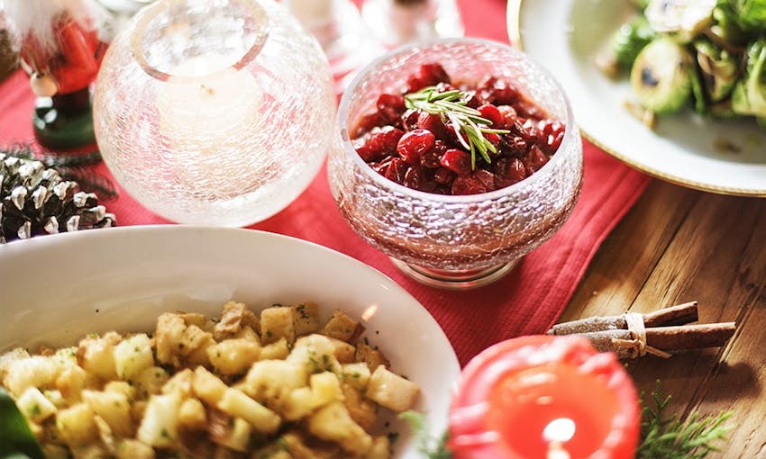 christmas dinner table with lit candle, brussel sprouts, side dishes and cranberry sauce topped with rosemary sprig 