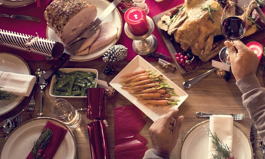 a table set and ready for christmas dinner complete with sliced meats, roast turkey, honey glazed carrots, sugar snap peas and christmas crackers 