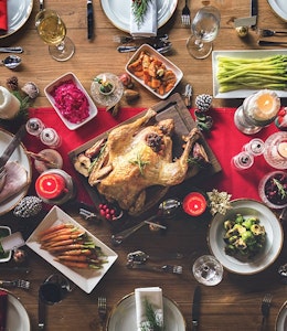 birds eye view of a fully set christmas dinner with a red table runner a turkey centre piece 