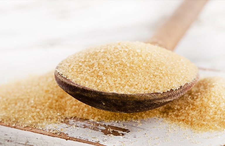 Brown sugar on a wooden spoon with sugar overflowing off spoon onto a wooden table 