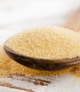 Brown sugar on a wooden spoon with sugar overflowing off spoon onto a wooden table 