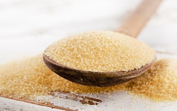 Brown sugar on a wooden spoon with sugar overflowing off spoon onto a wooden table 