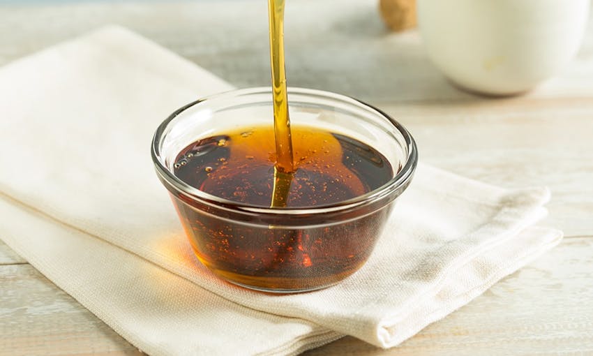 Agave syrup being poured into small glass pot in the middle of a cream napkin on a cream coloured tablecloth 